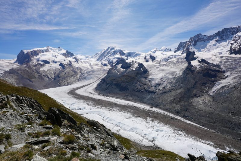 Snowcapped mountains under blue sky with river of white glacial ice in a valley.