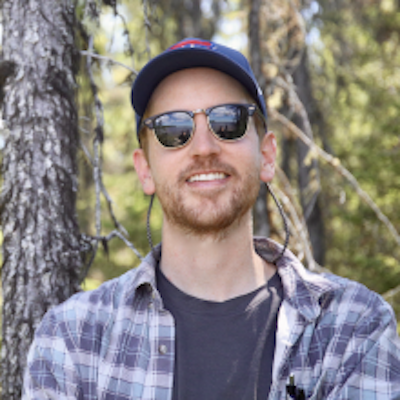 Smiling young man with sunglasses and trees behind him.