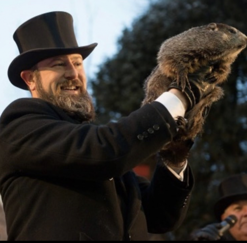 Man in top hat holds up a groundhog.