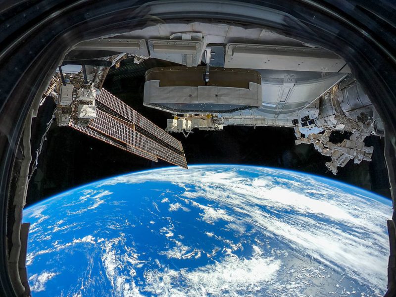 International Space Station: Metal trusses in black sky over curve of Earth and blue water with white clouds.