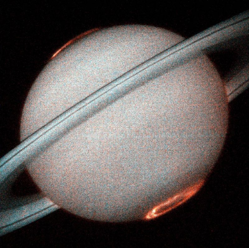 Saturn and rings in gray. Red auroras around both the north and the south poles.