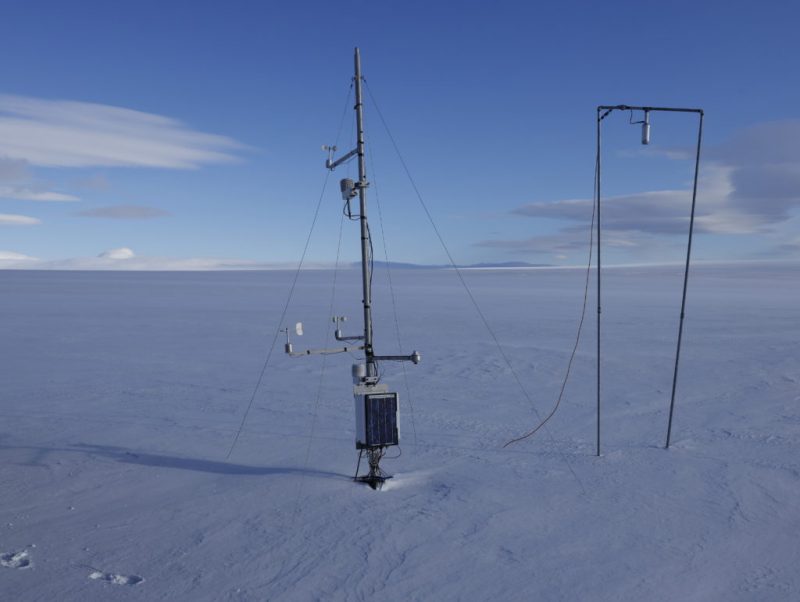 A long metal pole stuck in a field of ice under a blue sky.