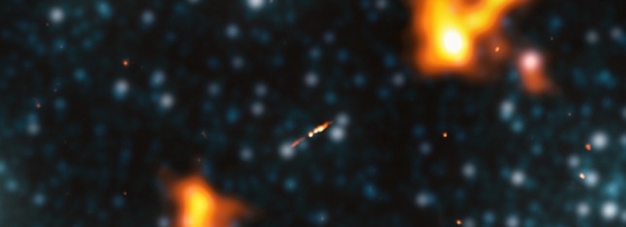 Largest galaxy yet: Small oblong light at center with two larger orange-yellow lobes, one on each side.