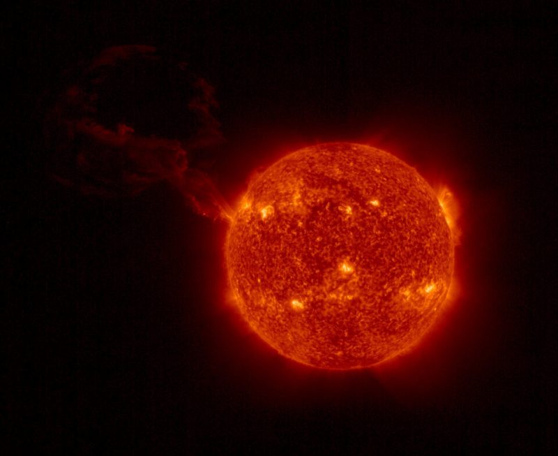 Solar prominence: Mottled orange circle of sun with bright spots and huge wispy filament extending outward.