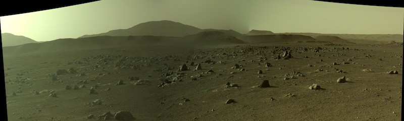 Brownish terrain with hills and ridges in the distance and dusty sky.