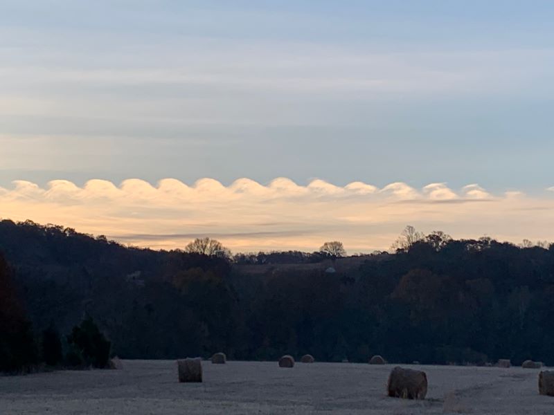 A dark scene with hay bales in front of a row of white rolling wave-like clouds in the background.