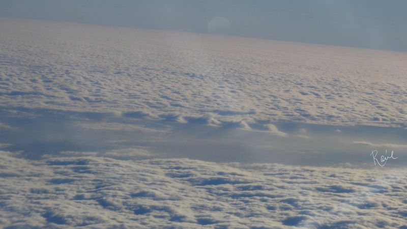 A view down at the clouds from an airplane. A gap in the clouds near the center shows wave-like clouds.
