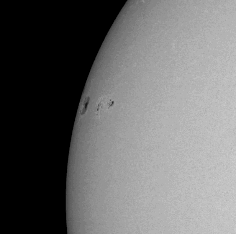 Part of a gray rotating globe with dark spots (sunspots) coming into view.
