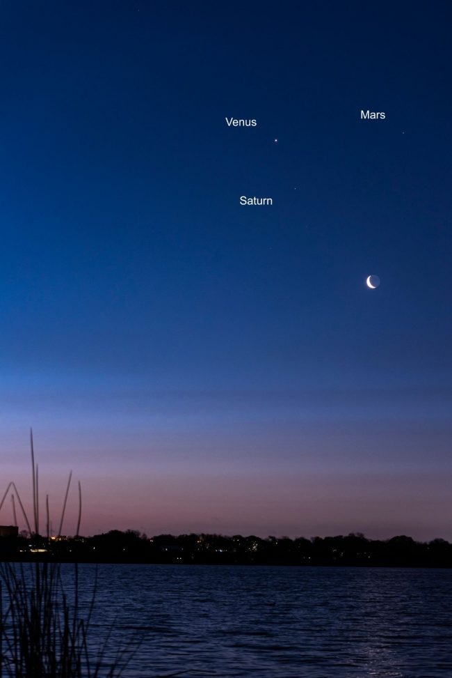 View of dawn over a lake, with the moon and three bright planets.
