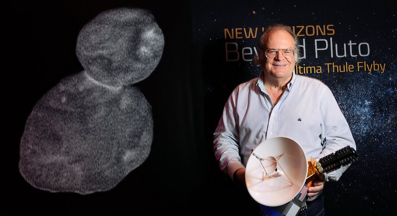Man holding a model of a spacecraft with a snowman-shaped asteroid to his left.