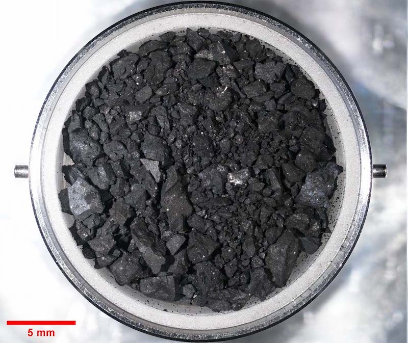 小惑星リュウグ：丸い金属容器に入れた暗い砂利と粉。