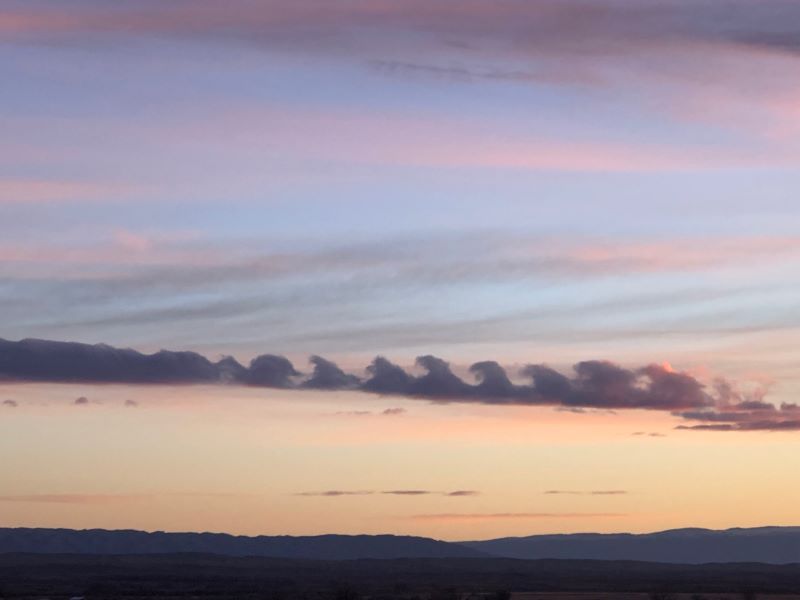 A sky with the colors of sunrise and dark clouds shaped like waves.