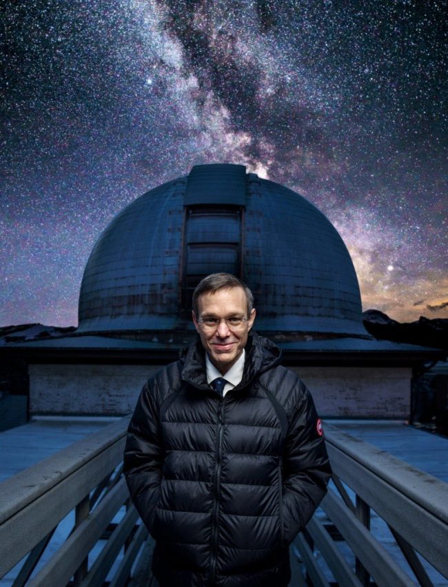 Man standing in front of observatory dome with Milky Way behind.