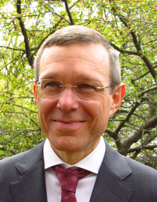 Smiling middle-aged man in suit and tie with tree behind him.