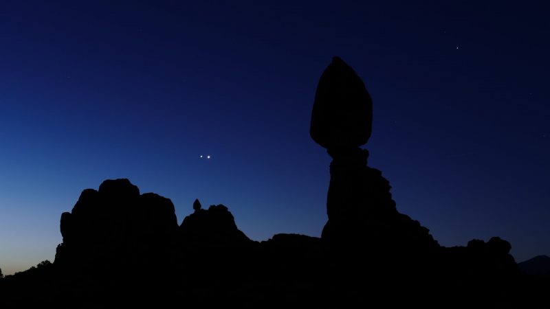 Two bright planets at dawn right above a rock formation.