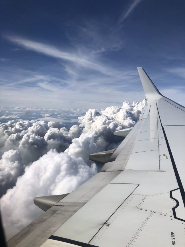 Bumpy flight: Towering, billowing cumulus reaching plane wing with thin whitte streaks above in blue sky.