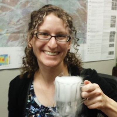 Smiling young woman with curly hair holding a glass mug.