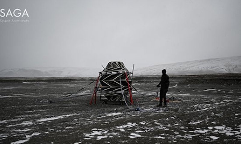 Small egg-shaped structure on rocky frozen ground with man standing next to it.