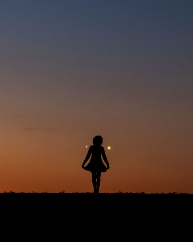 Woman's silhouette at dawn with two bright planets behind.