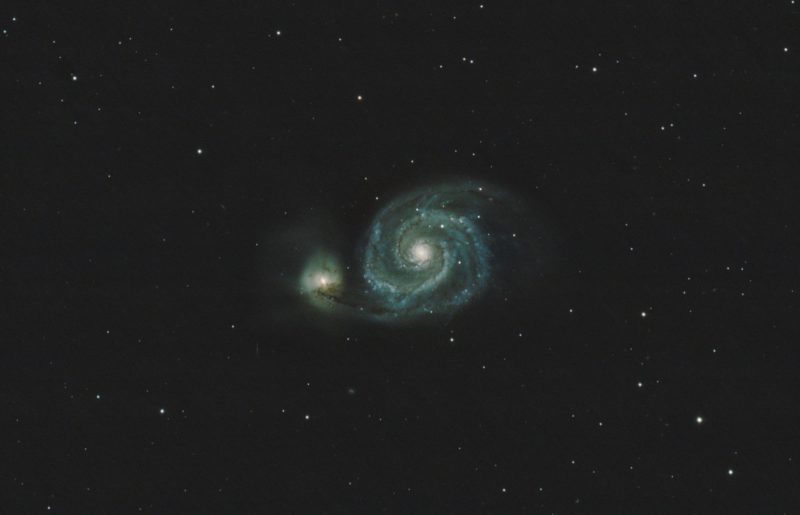 A greenish spiral in star field with brighter center, and a bright detached area to its left.