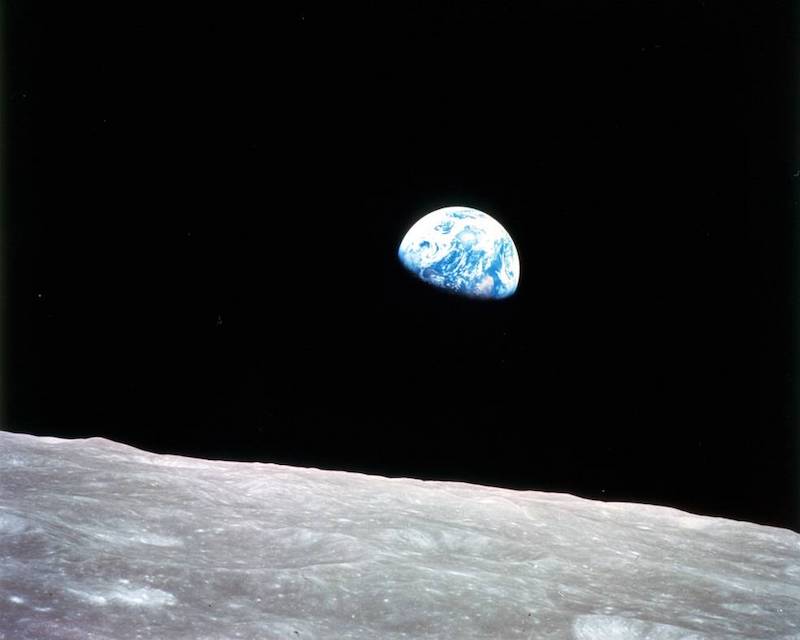 Earth Day: A blue half-sphere shape with white swirls stands out against blackness with a gray and rocky piece of foreground.