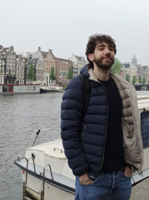 A happy-looking young man standing next to a Dutch canal lined with ancient houses.