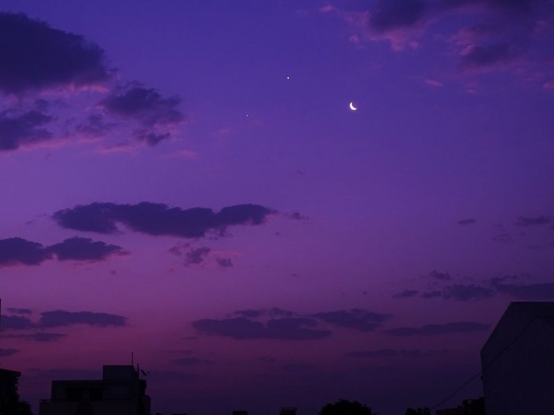 Venus, Jupiter and the moon in a purple sky with some clouds.
