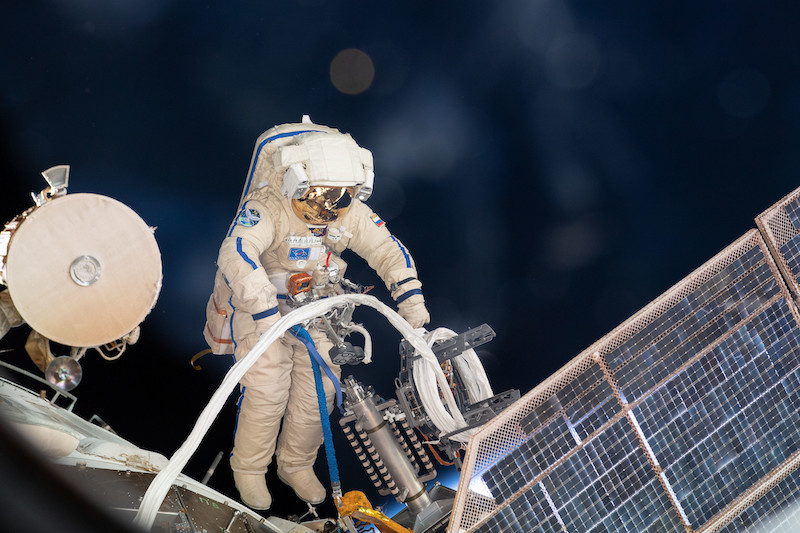 Spacewalk: A person in a bulky white spacesuit is posed near ISS external cables and solar panel.