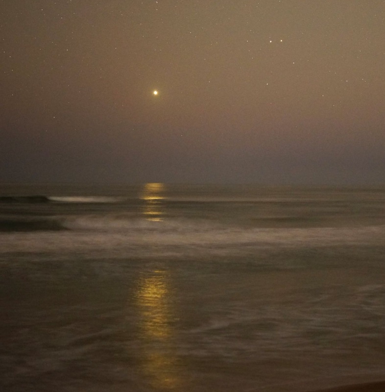 Venus, and close Mars and Saturn in yellow sky over ocean.