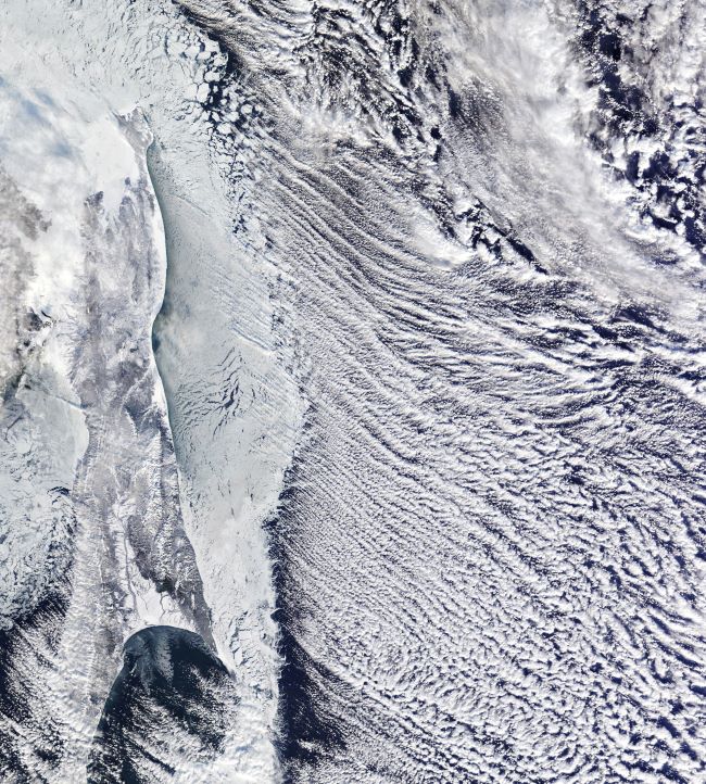 Satellite image showing thin rows of clouds streaming away from a body of water.