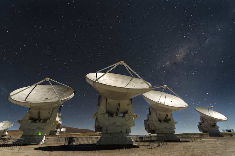 Five dish-shaped radio telescopes pointing toward starry sky above.