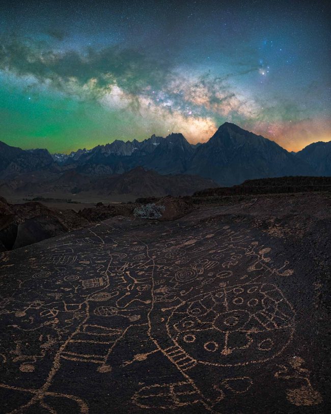 Greenish sky with Milky Way and rock art in foreground.