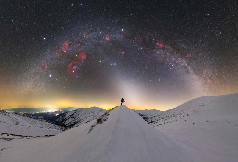 Best Milky Way: Tiny man standing on snowy peak with Milky Way arching overhead.
