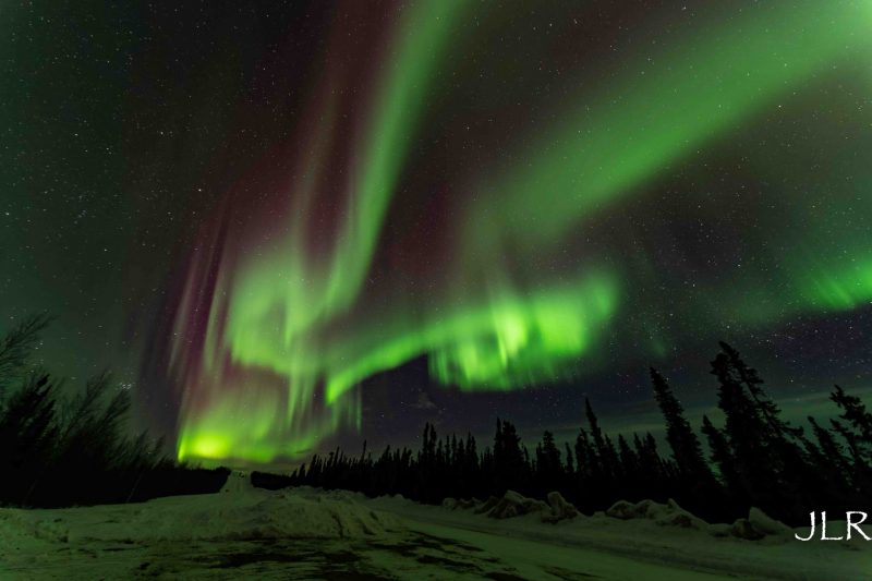 Swirls of neon-green aurora in a dark sky over winter landscape.