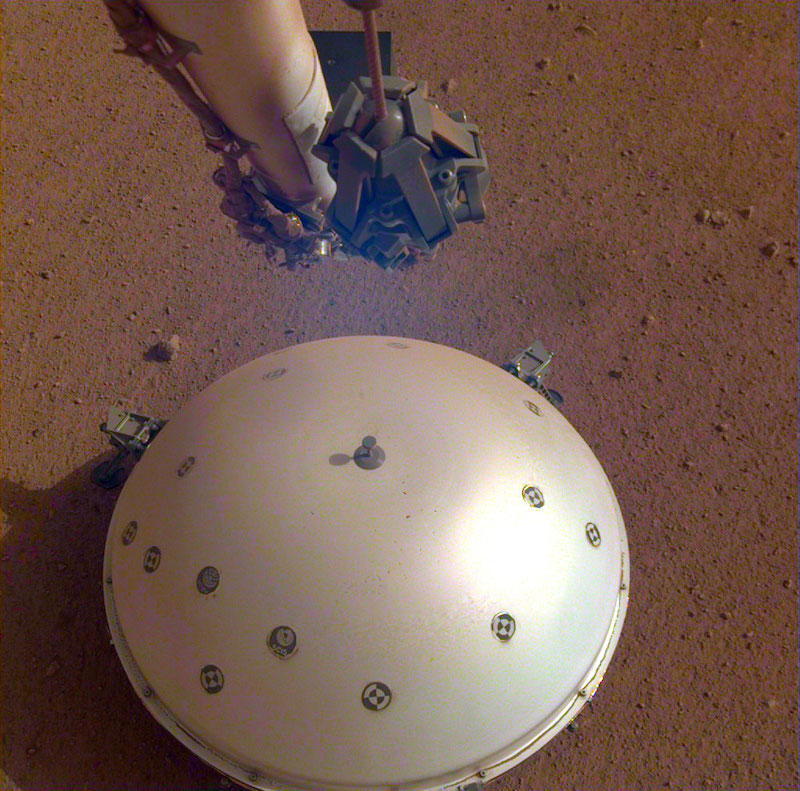 Shiny dome sitting on reddish soil with robotic arm above it.
