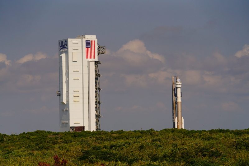 Rocket on launch pad, awaiting launch, with huge vertical assembly building nearby.