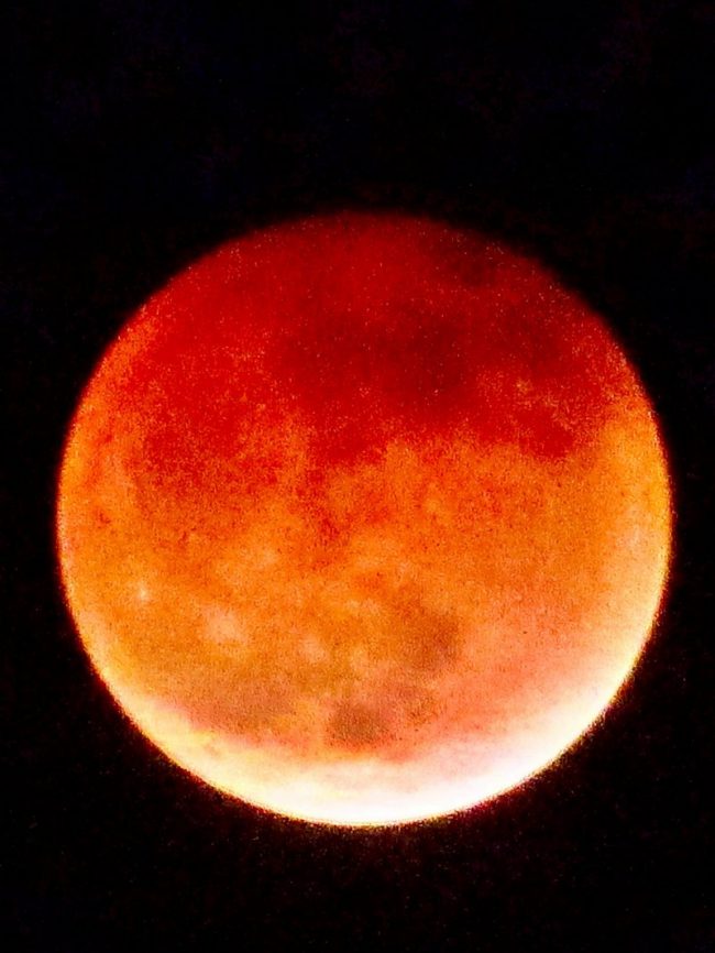 Large, somewhat fuzzy moon mostly red with white area at bottom.