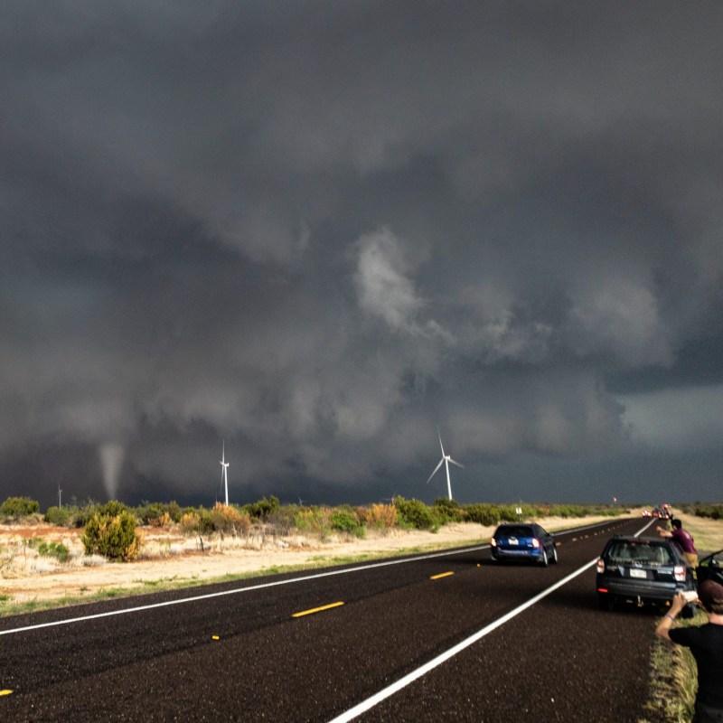 Storm chasing: People on side of road taking pictures of a tornado under lowering dark clouds.