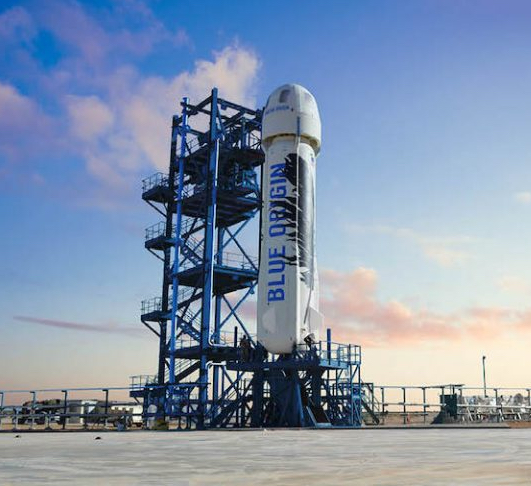 Large white rocket standing next to multilevel gantry against blue sky.