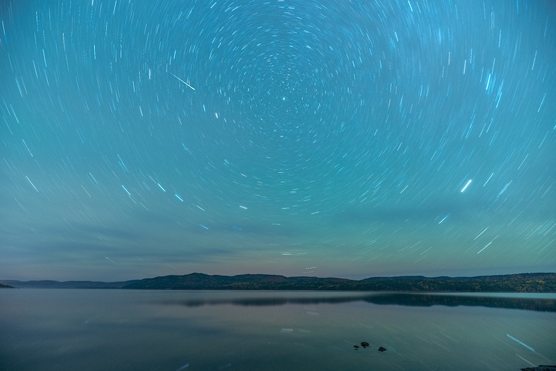 Nigiht sky with circular star trails around north star and a meteor streak on the sky.