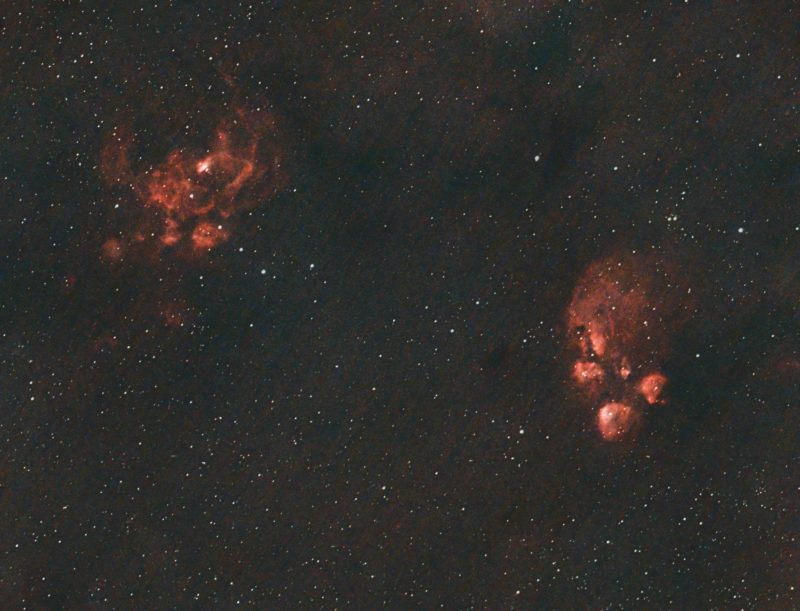 Two patches of red nebulous light over a background of distant stars.