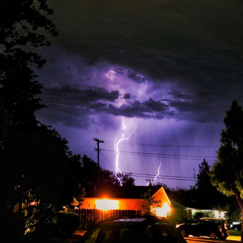 Lightning storm with clouds and purple glow, house lit up in foreground.