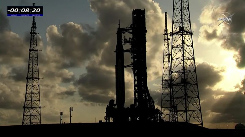 Launches: Silhouette of tall rocket next to gantry tower.