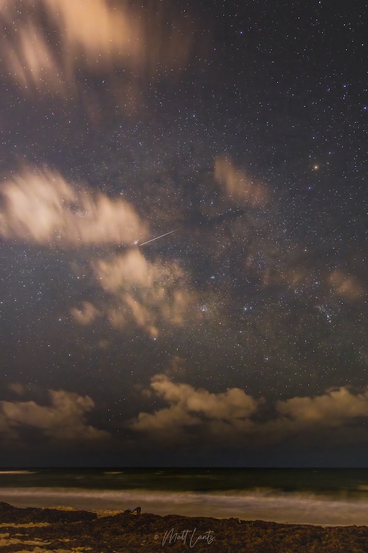 Clouds and a white streak against a starry sky.