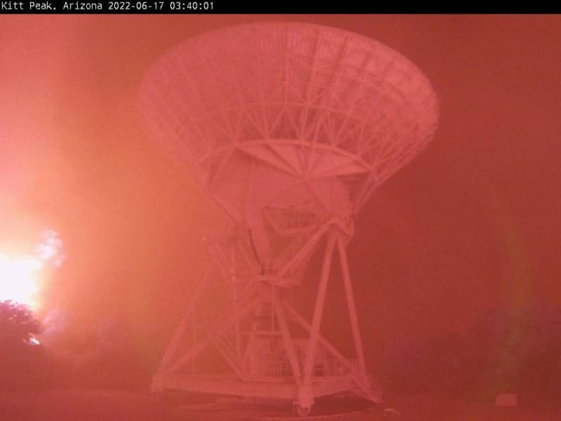Kitt Peak: Radio telescope dish in deep red haze with bright fire on left.