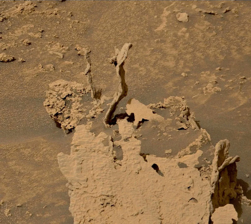 Curiosity rover: 2 small spikes of rock protruding above surrounding rock and sand.