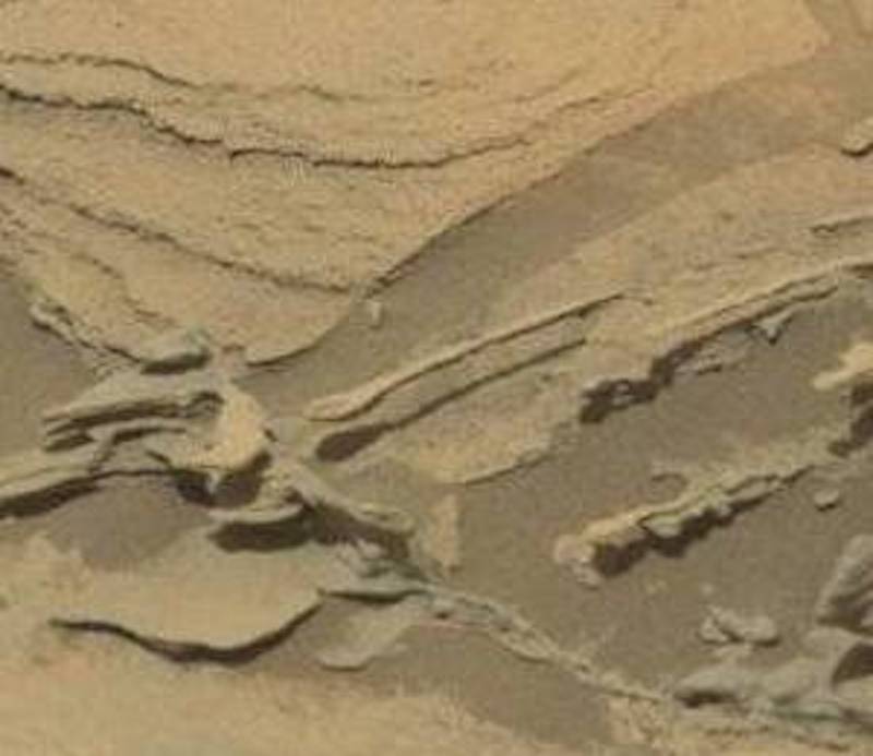 Spoon-shaped rock attached to a larger flat rock on reddish terrain.