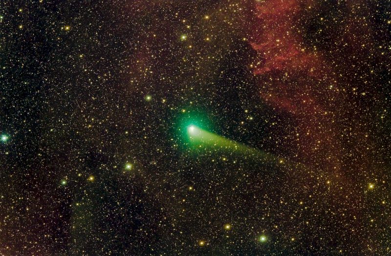Greenish comet head with streaking tail in very dens star field and faint nebulae.