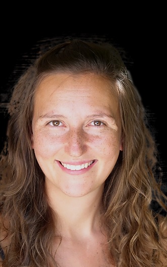 Young woman with freckles and wavy brown hair smiles at the camera.