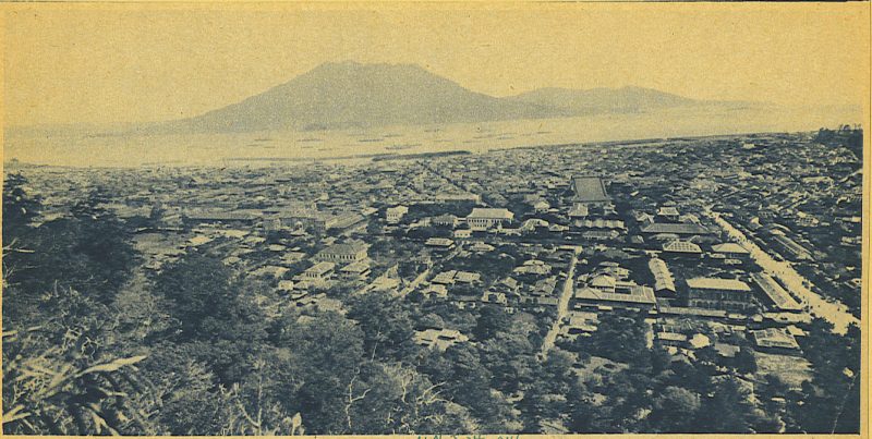 Old photo of large, old-style Japanese city covered in ash, with volcano visible in the distance.